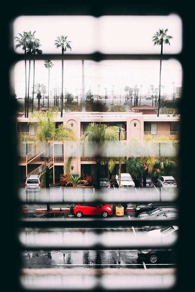 View through the window blinds on the parking lot, palm trees and two story residential building. Original public domain…