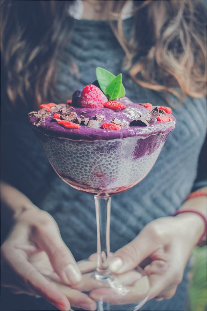 A woman holding purple Chia Pudding covered with berries and mint leaves in a glass cup in the Lima Region. Original public…