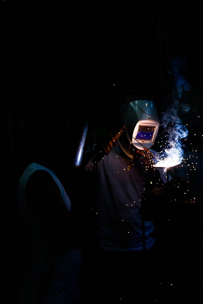 Two people weld in the dark in Nejapa. Original public domain image from Wikimedia Commons