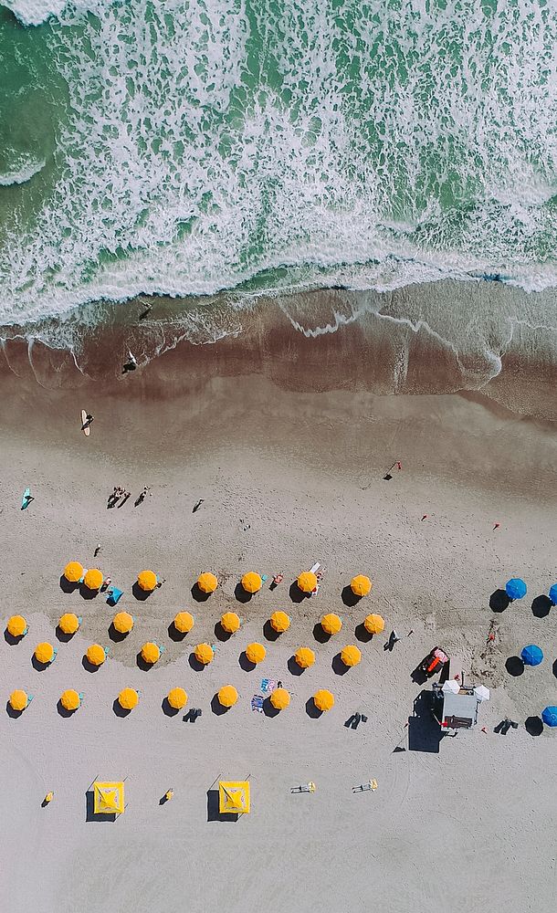 An aerial shot of a sandy beach with rows of yellow and blue umbrellas. Original public domain image from Wikimedia Commons