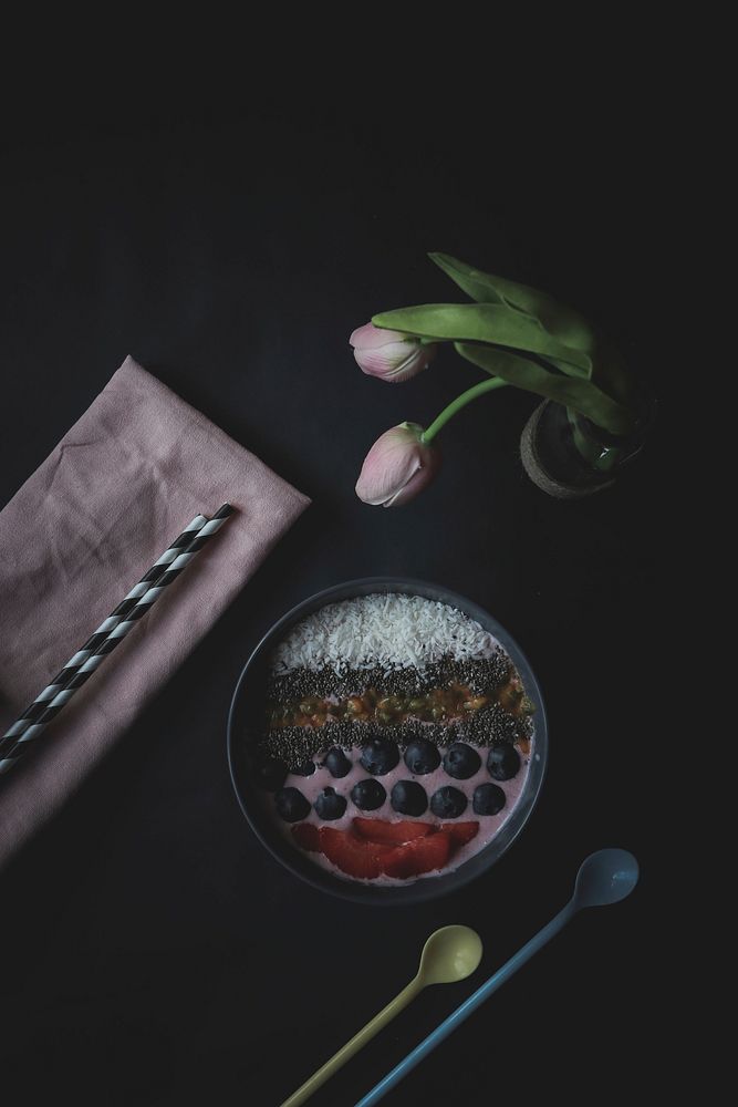 A flat lay shot of a fruit dessert, a vase of roses, spoons, straws, and napkin. Original public domain image from Wikimedia…