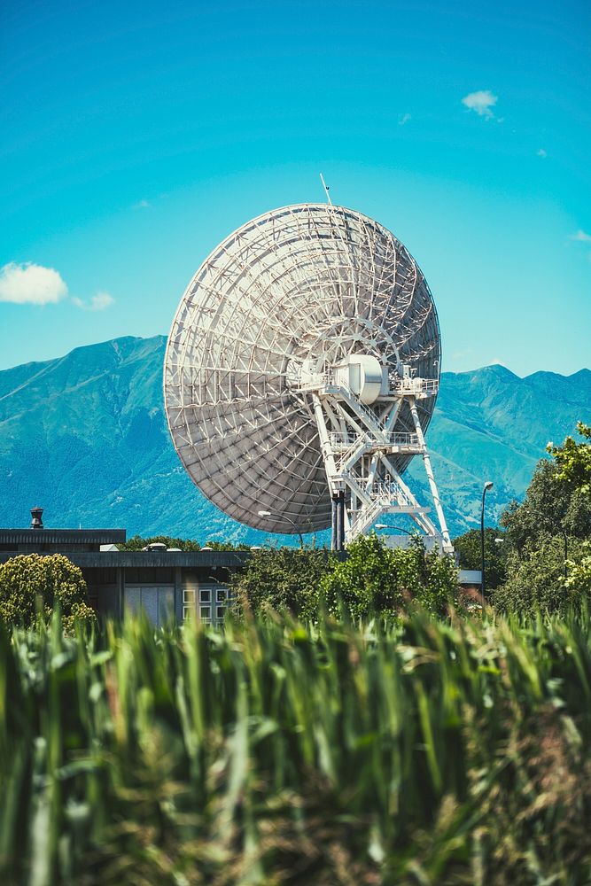 Communication satellite in a grassy field near the mountains. Original public domain image from Wikimedia Commons