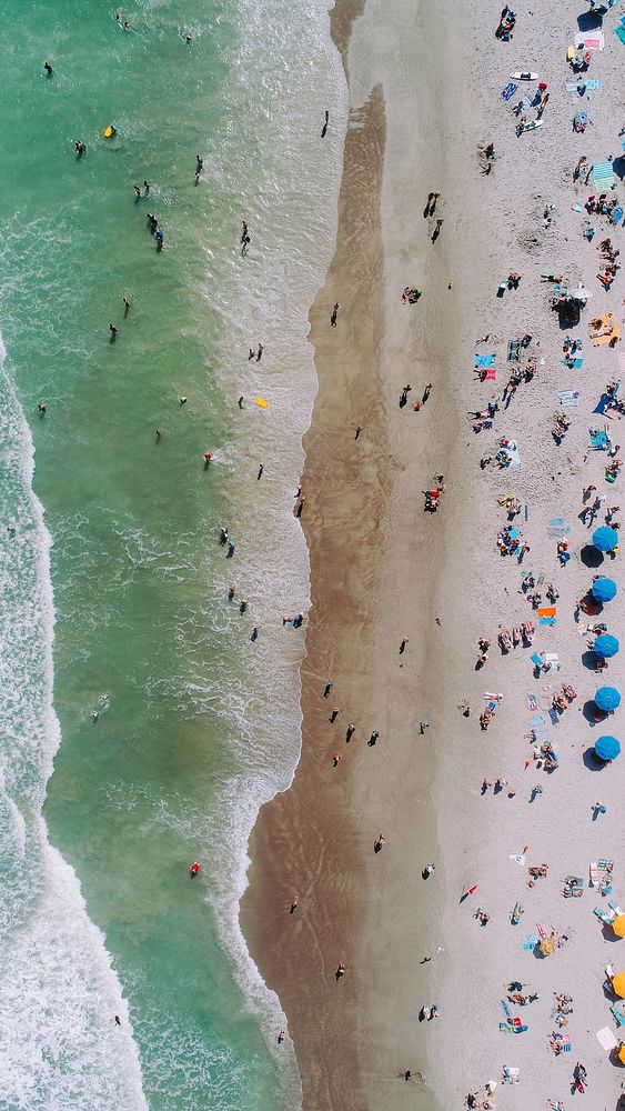A drone shot of waves breaking on the edge of a crowded golden beach. Original public domain image from Wikimedia Commons