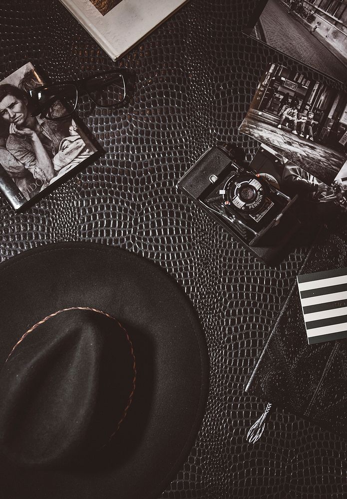Vintage shot of hat, camera, glasses and monochrome photos lying on leather surface. Original public domain image from…