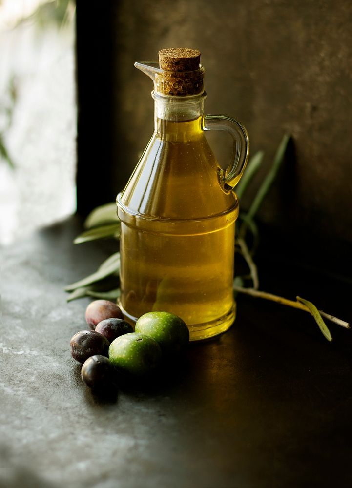 A glass jug of extra virgin olive oil next to some fruit on a table. Original public domain image from Wikimedia Commons