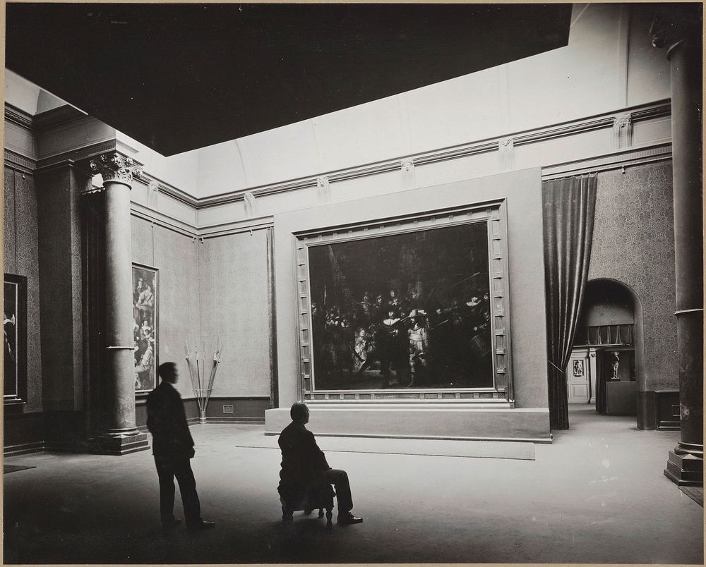 Zaal met De Nachtwacht op een paneel voor een muur, vooraan een staande en een zittende man (1929) by Rijksmuseum Afdeling…