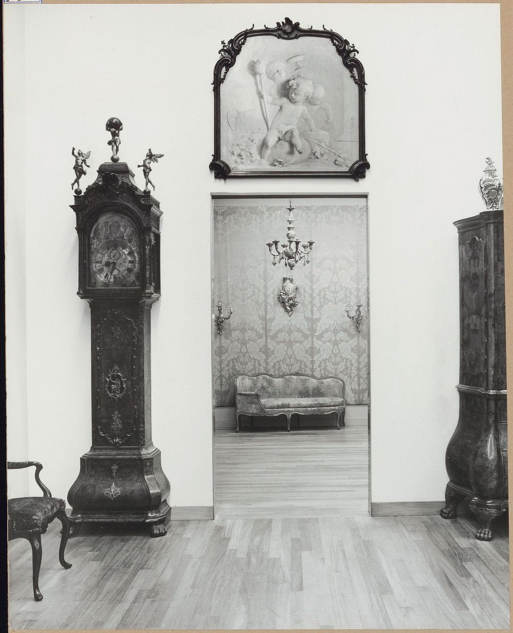 Zaal met staande klok, kast en grisaille boven een doorgang naar zaal met wanddecoratie en bank (1962) by Rijksmuseum…