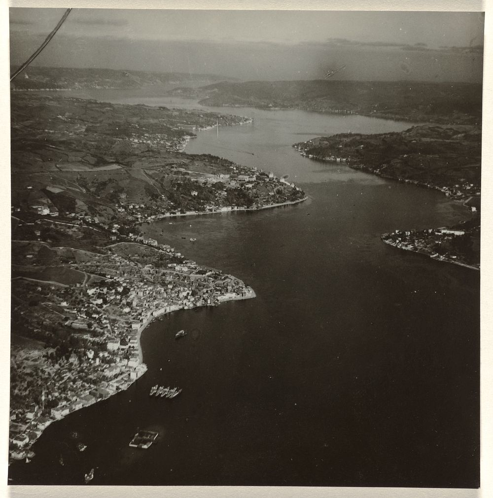 Luchtfoto in zwart-wit van een stad of dorp, gelegen aan een rivier of baai, met inhammen in de rivier of baai en boten en…