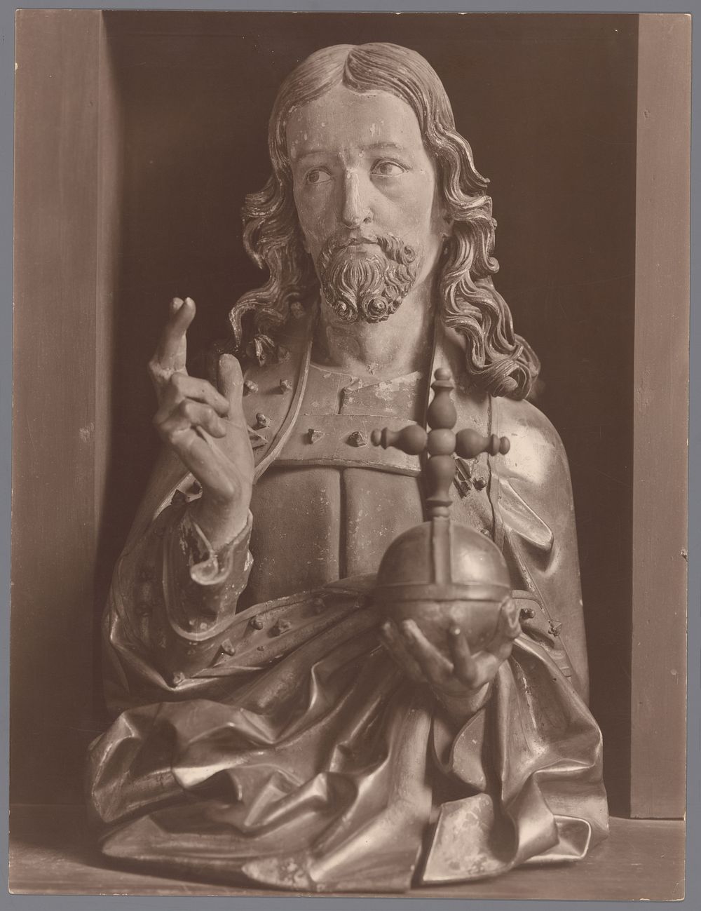 Gezicht op een buste van Christus die met de ene hand een zegenend gebaar maakt en in de andere hand een rijksappel draagt…
