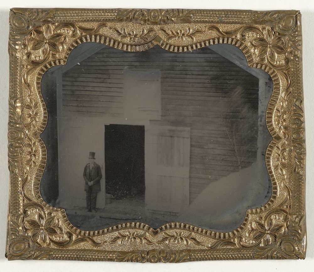 Man staand bij de open deur van een houten schuur (1870 - 1900) by anonymous
