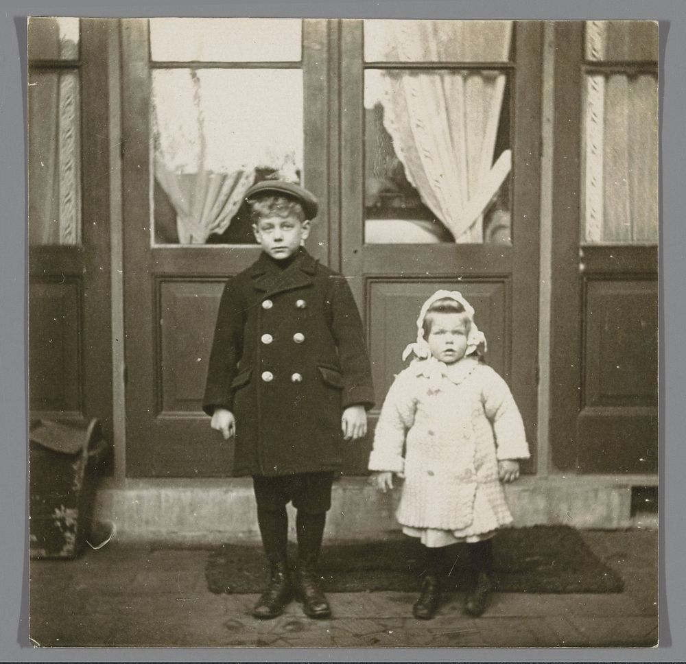 Portret van twee onbekende kinderen, staande voor een deur (c. 1905 - c. 1910) by anonymous