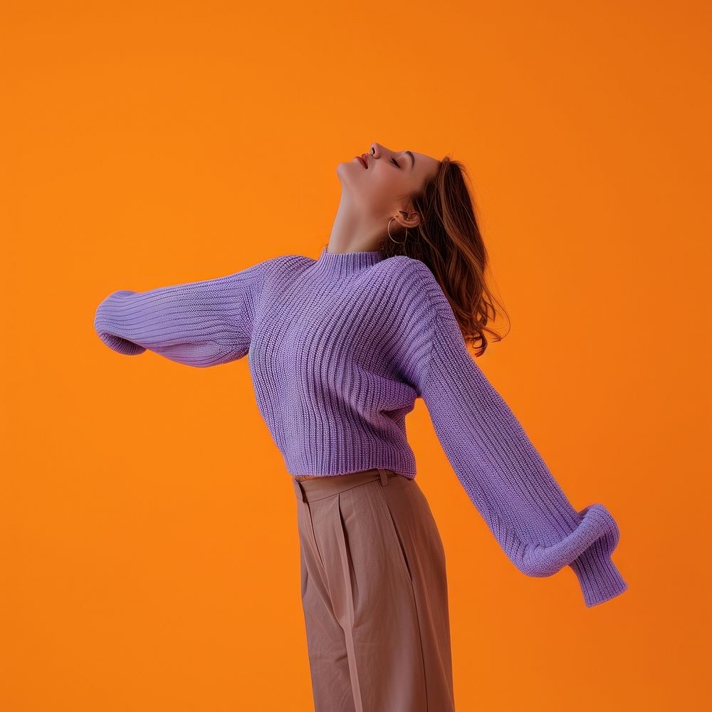 Woman in purple sweater with her arms open orange background hairstyle standing.