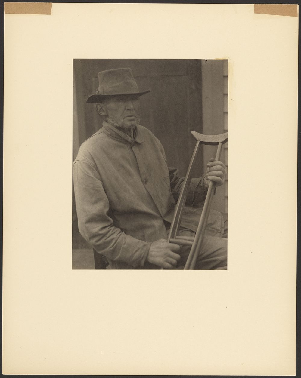 Seated Man Wearing Hat and Holding Crutches by Doris Ulmann