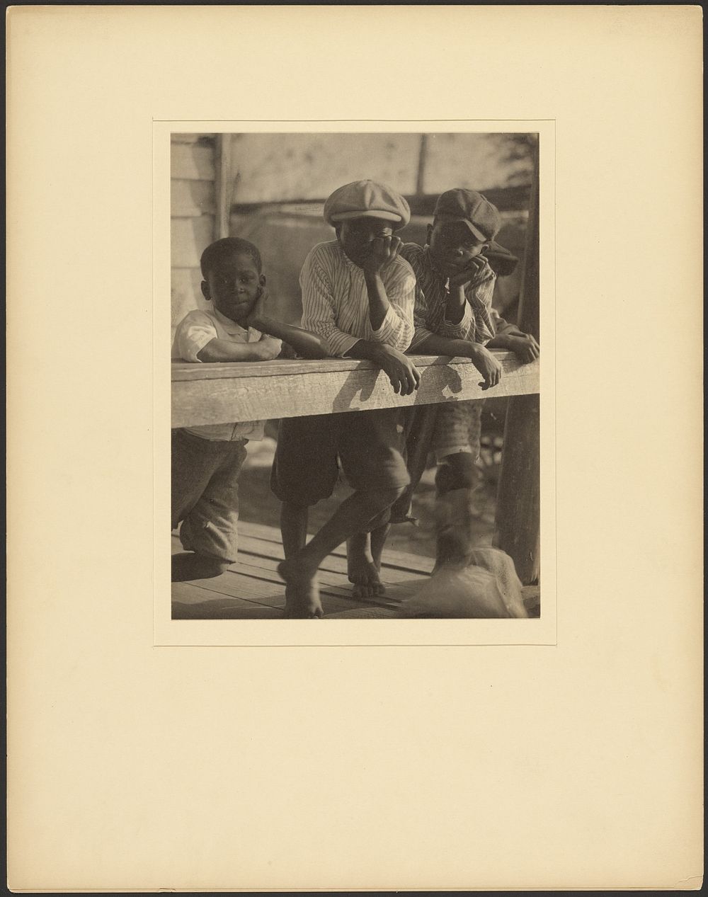 Three Black Boys Leaning Over Wooden Railing by Doris Ulmann