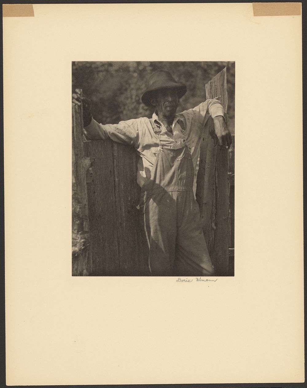 Man in Overalls Leaning Against Old Fence by Doris Ulmann
