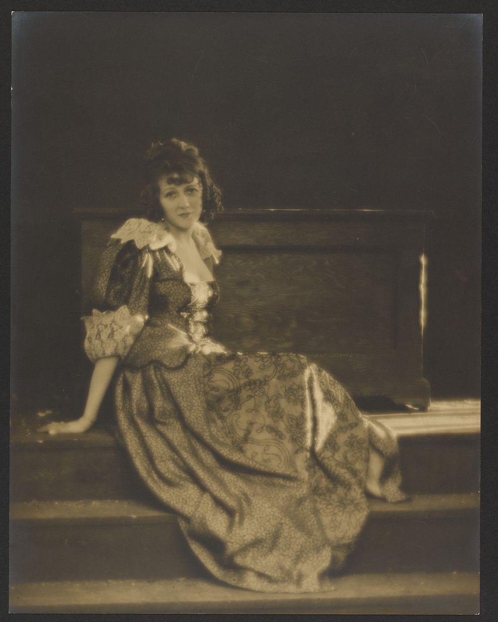 Barbara La Marr in Peasant Costume Seated on Stage Step with Large Wooden Box Behind Her by Arthur F Kales
