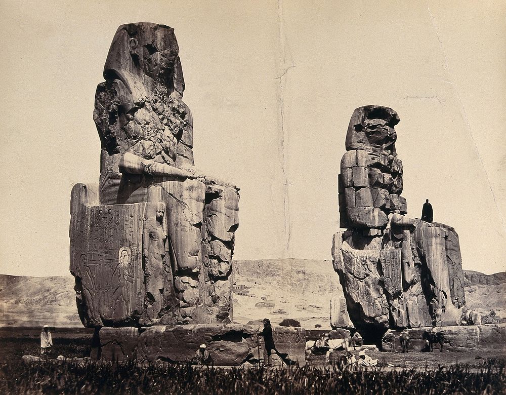The Statues of the Plain, Thebes, Egypt: a man is standing in the lap of one statue; other men and donkeys at the base.…