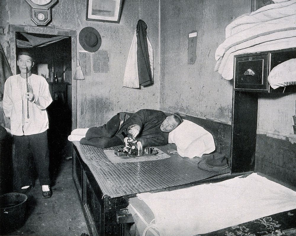 An opium den in San Francisco, early 20th century, with two Chinese men smoking. Process print after a photograph.