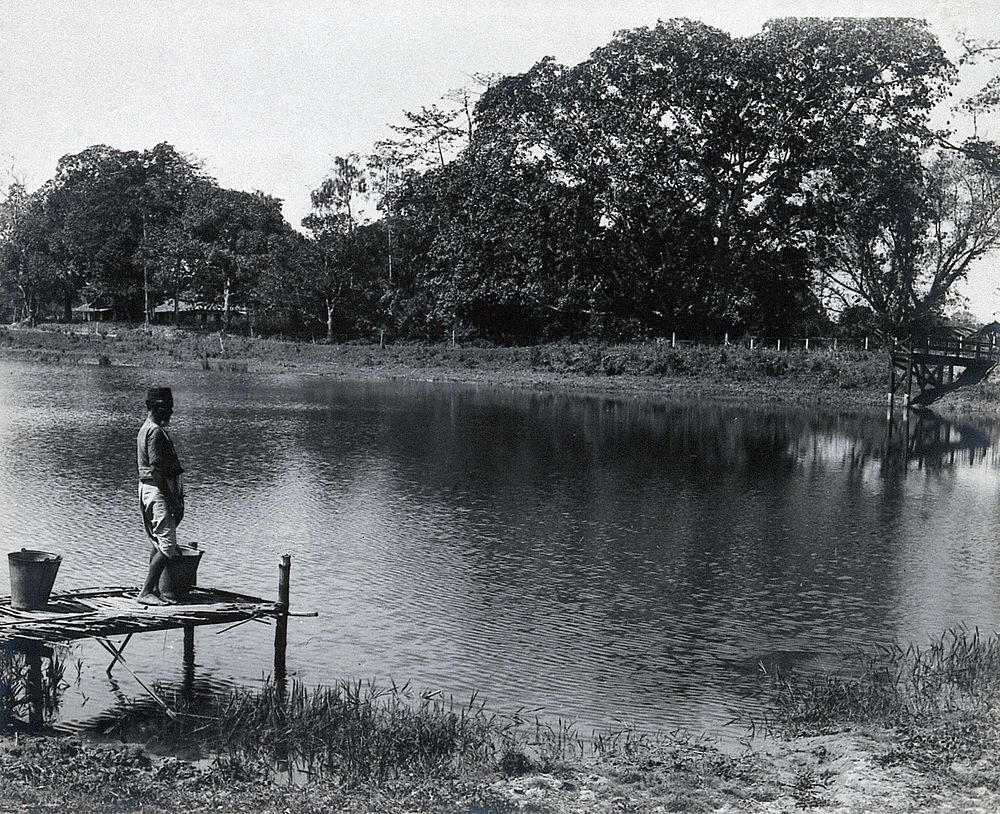 A reservoir, India: an Indian man stands with two buckets on the jetty. Photograph, 1910/1920 .