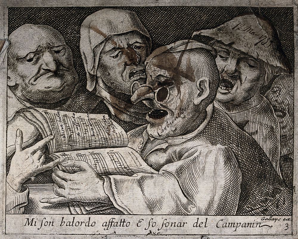 A man wearing spectacles is singing from the songbook he is holding as three others join in and a fourth man keeps his mouth…