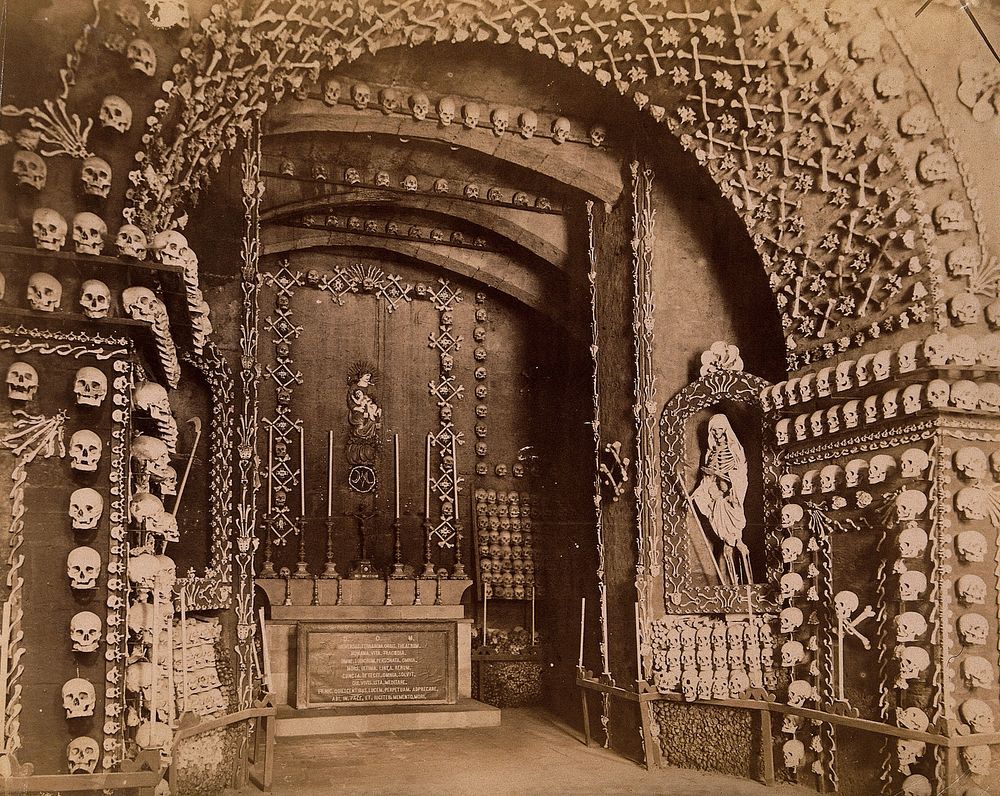 An altar bearing a Latin inscription surrounded by an array of human skulls and bones and a cloaked skeleton. Photograph by…