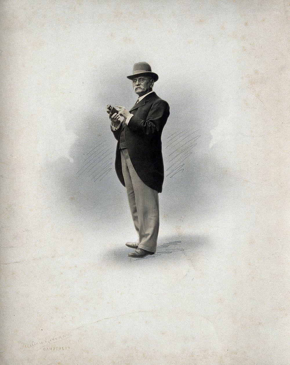An unidentified man, full-length, holding a camera  . Photograph by Frederic Robinson.
