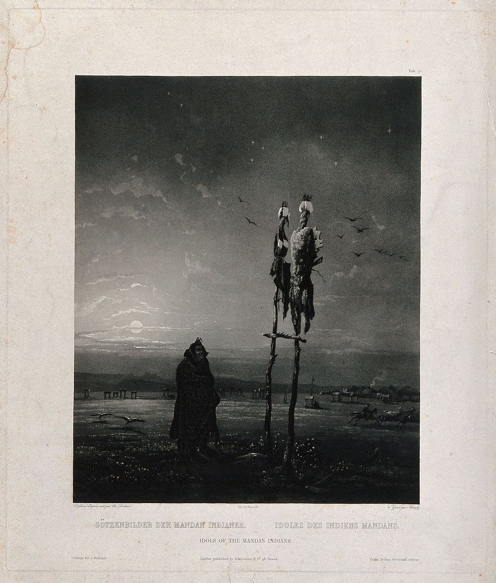A man from the Mandan tribe is looking up at two idols placed on wooden sticks; a village in the background. Aquatint by S.…