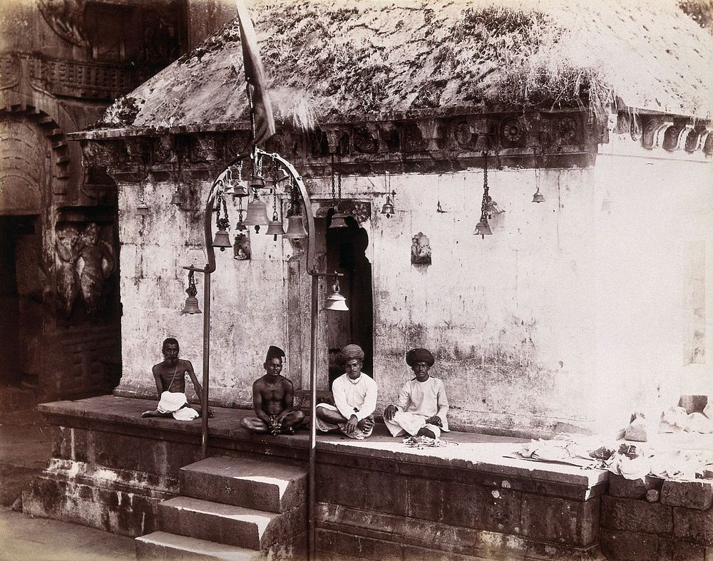 Four men sitting cross-legged outside a building with bells hanging from the roof: Bombay at the time of the plague.…