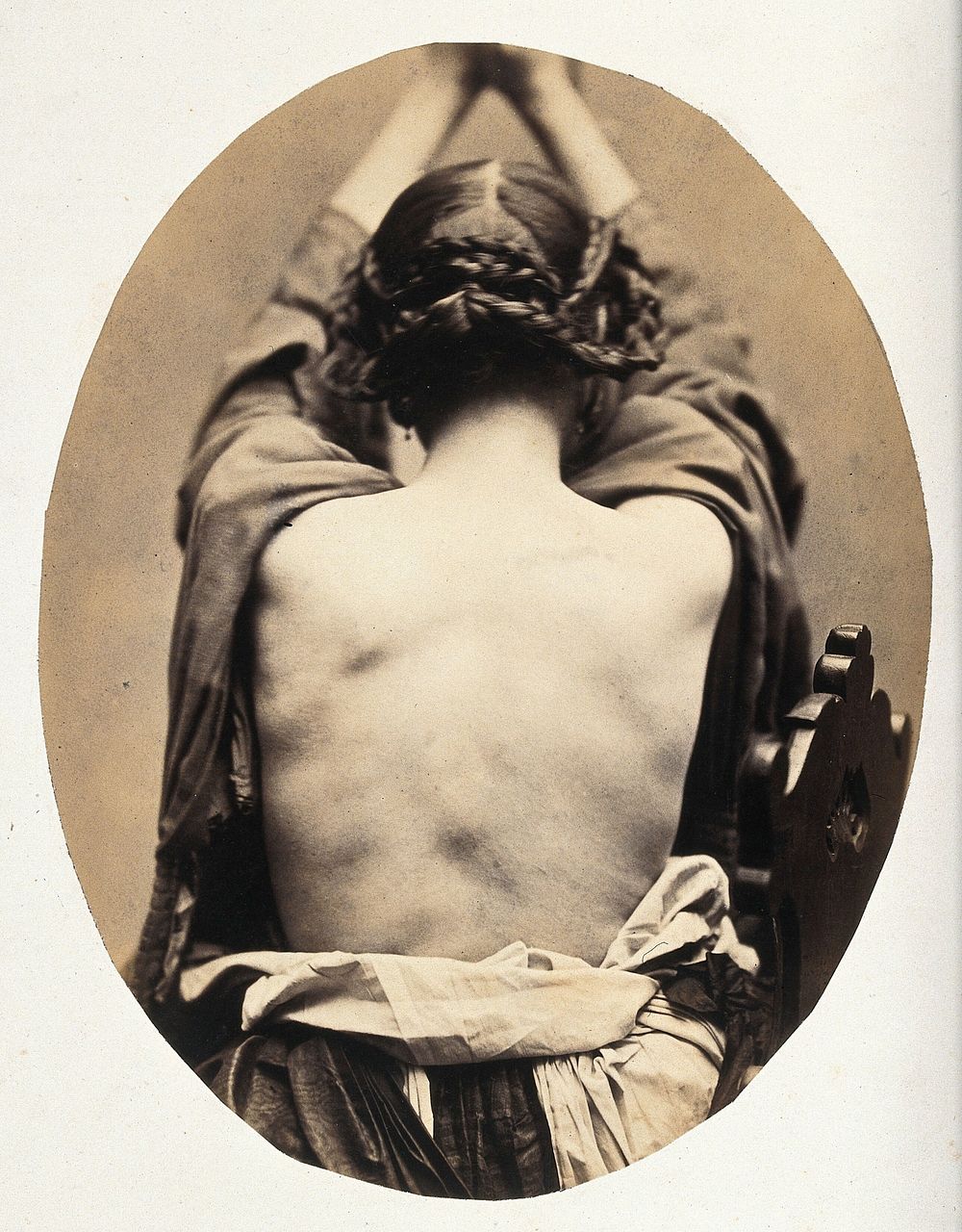 A woman, viewed from behind with open dress revealing back; she is holding her arms up. Photograph by L. Haase after H.W.…