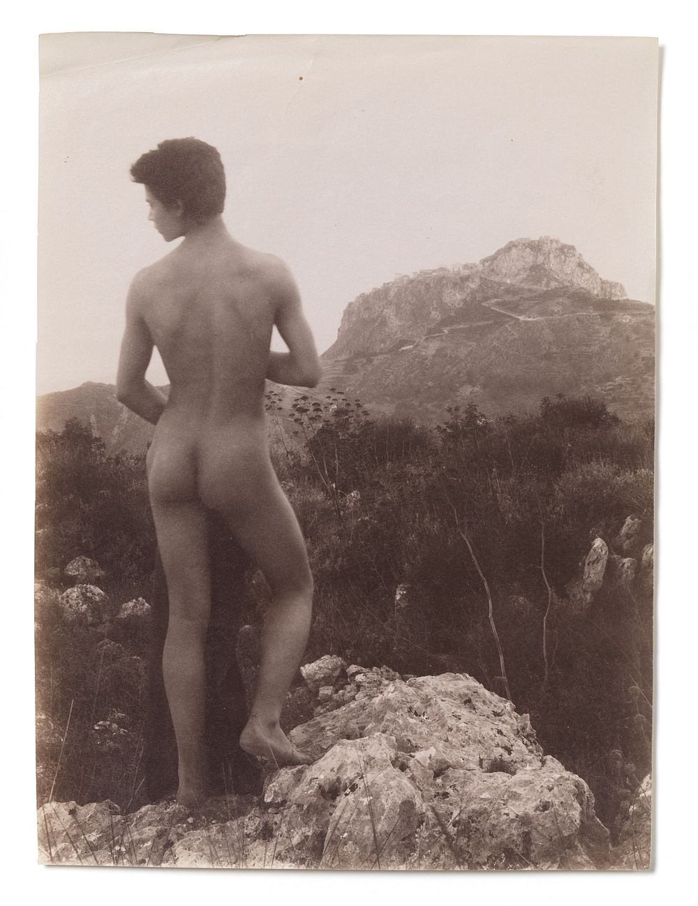A naked Sicilian boy, in a rocky setting outdoors. Photograph, 1900, by W. von Gloeden.
