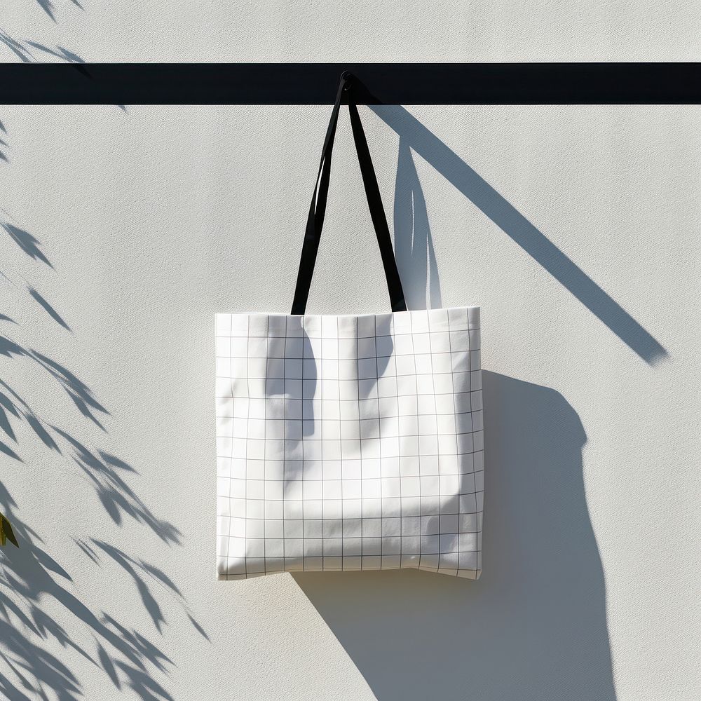 A white fabric tote bag is hanging on a black grid fence handbag wall accessories.