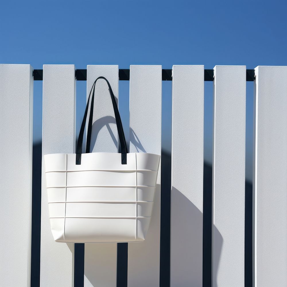 A white tote bag is hanging on a black grid fence handbag wall blue.