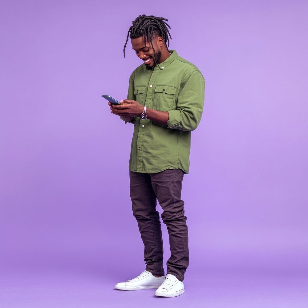 An isolated black man wearing green shirt playing his phone with smile purple photography background.