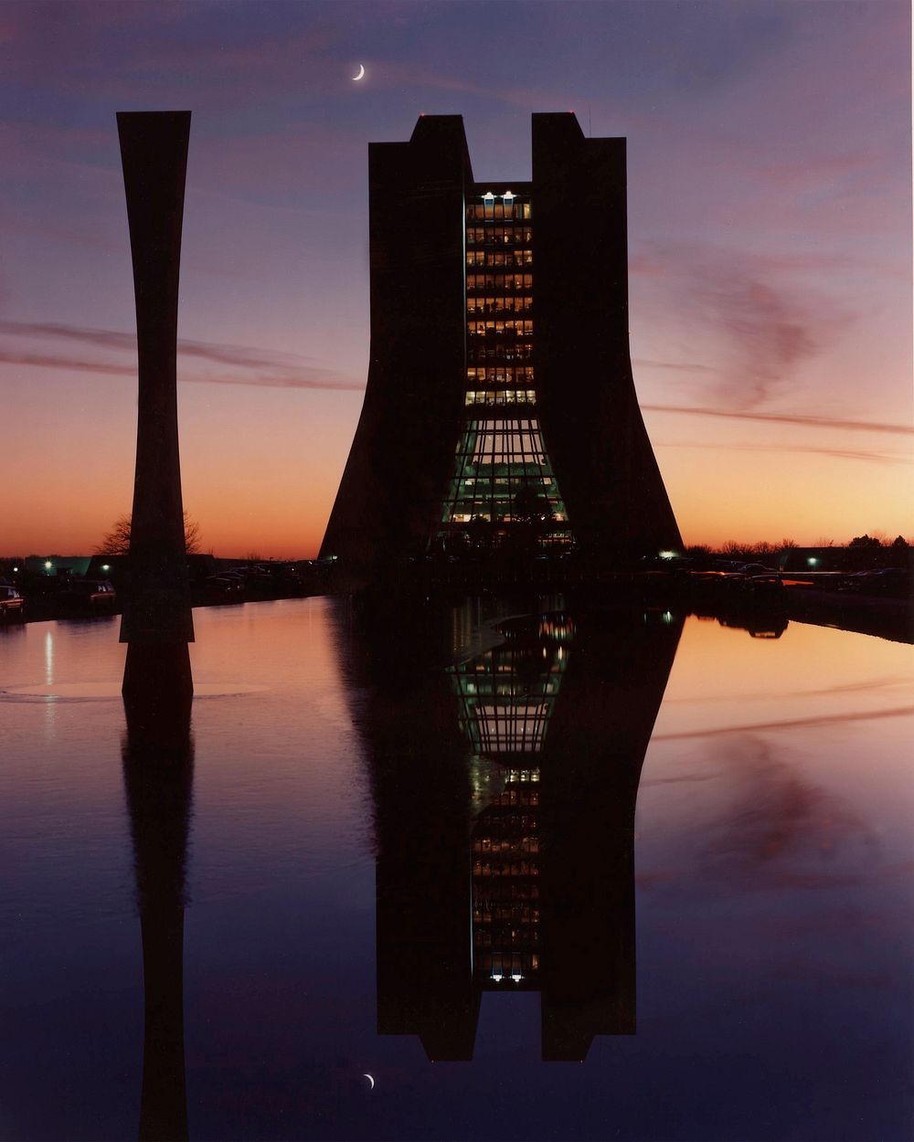 Night, in the form of a crescent moon, overtakes the fading light of day beyond Wilson hall at Fermi National Accelerator…