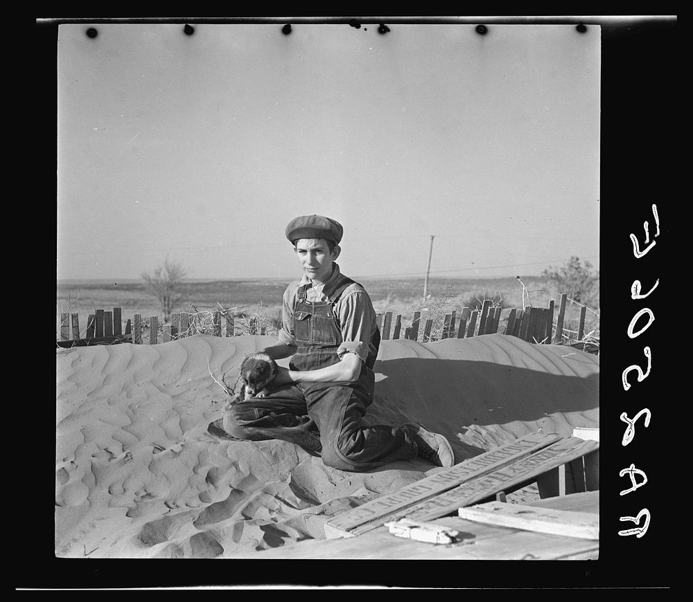 A farmer's son playing on one of the large soil drifts which threaten to cover up his home. Liberal, Kansas. Sourced from…