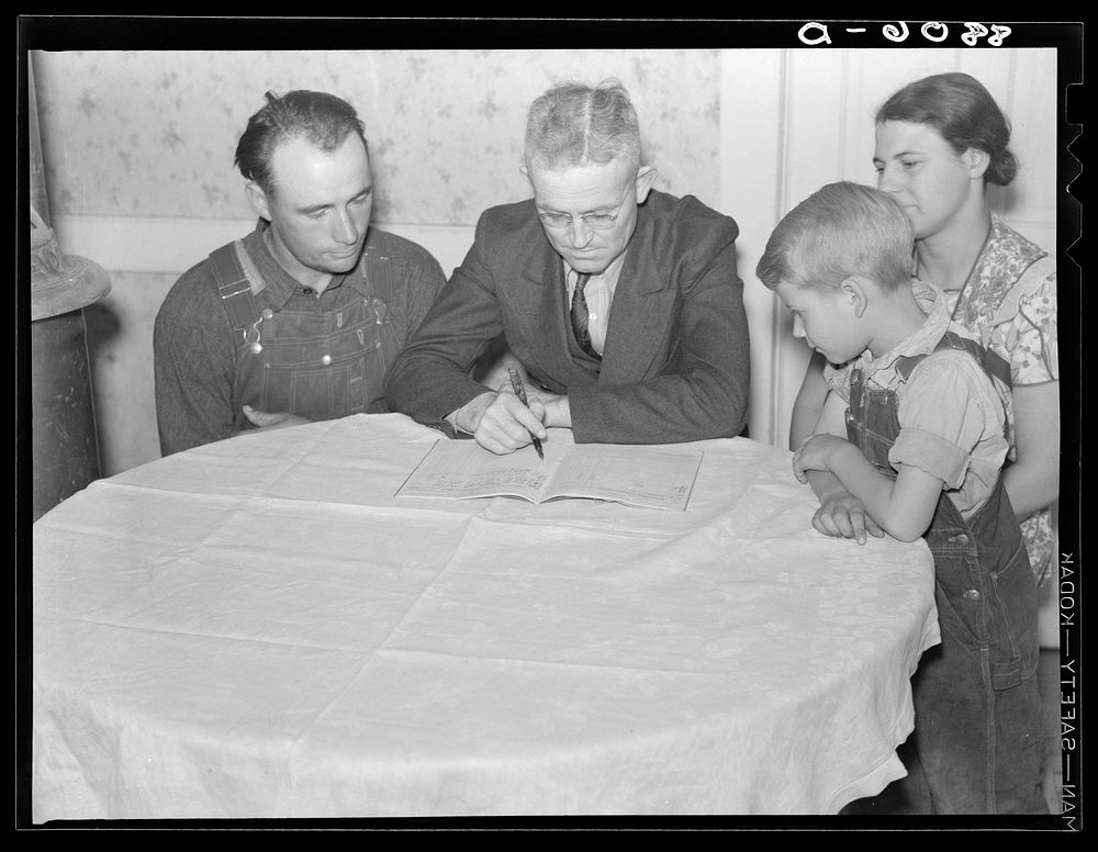 County supervisor helping rehabilitation family with account book. Dawson County, Nebraska. Sourced from the Library of…