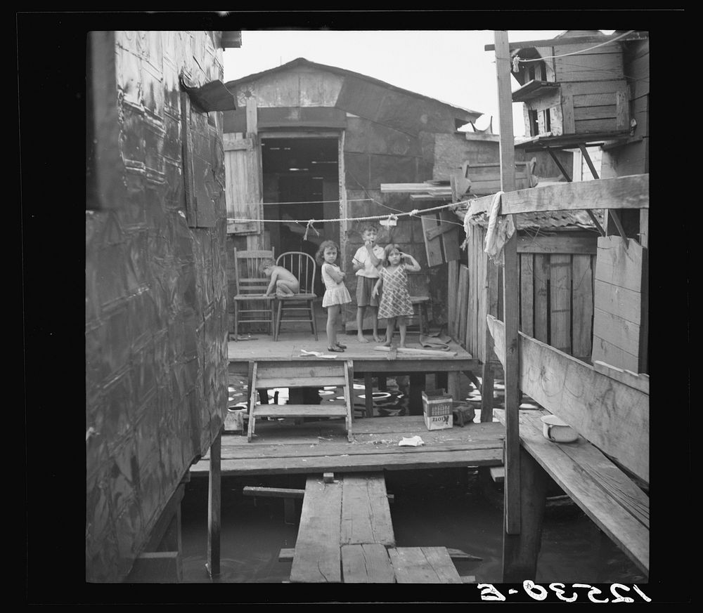 Slum dwellings in the workers' quarter of Porta De Tierra. Note: shacks are built on piles driven into swamp. Under the…