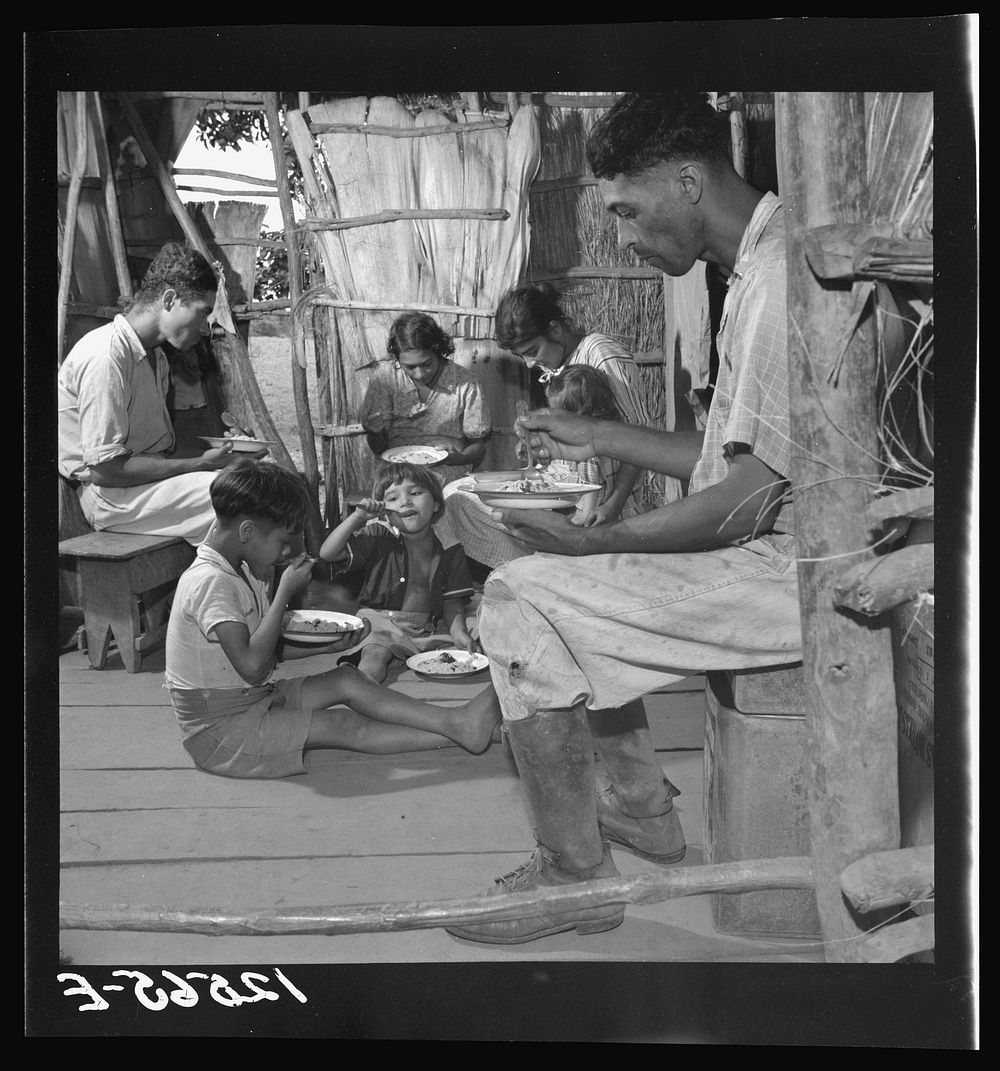 Jibaro family eating their main meal: rice, beans and a few pieces of codfish. Near Cidra, Puerto Rico. Sourced from the…
