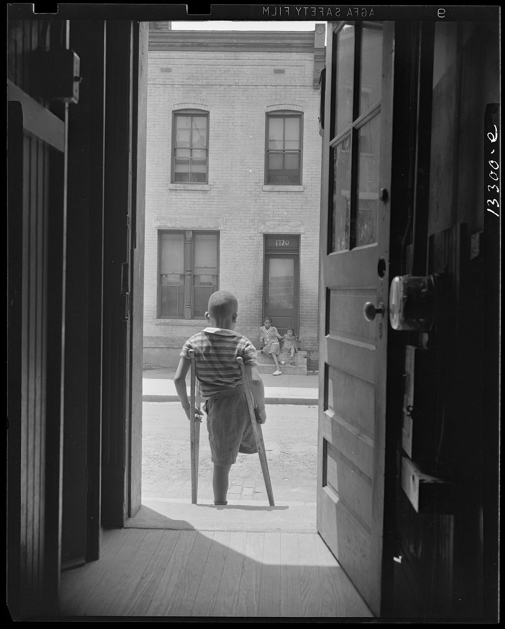 Washington, D.C. Young boy standing in the doorway of his home on Seaton Road in the northwest section. His leg was cut off…