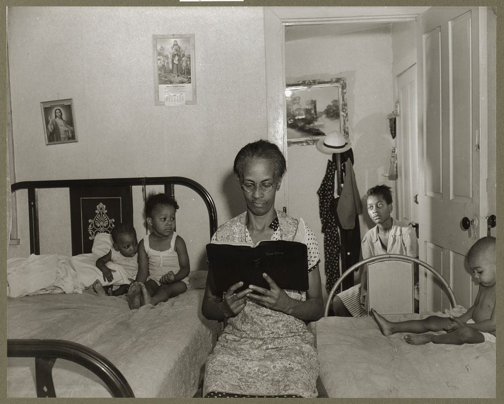 Washington, D.C. Mrs. Ella Watson, a government charwoman, reading the Bible to her household. Sourced from the Library of…