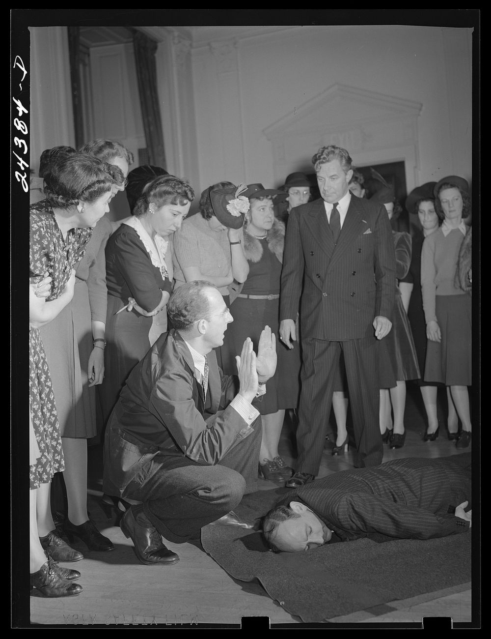 Civilian defense volunteers receiving instruction in proper care for man with spine injury. First aid class. American Red…