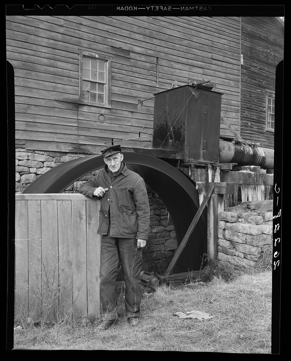 Willard Perdew, old resident of Chaneysville, Pennsylvania, standing in front of 100 year-old grist mill that is still in…