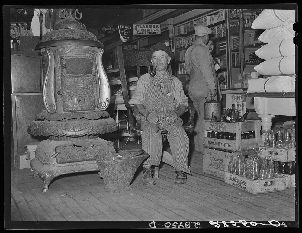 Farmer sits near the stove. General store. Lamoille, Iowa. Sourced from the Library of Congress.