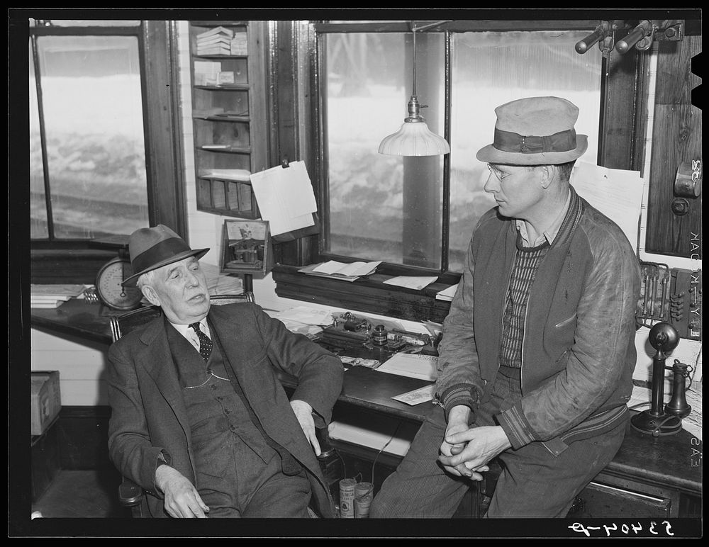 Ticket agent and mail carrier talking in railroad station. Mount Whittier, New Hampshire. Sourced from the Library of…