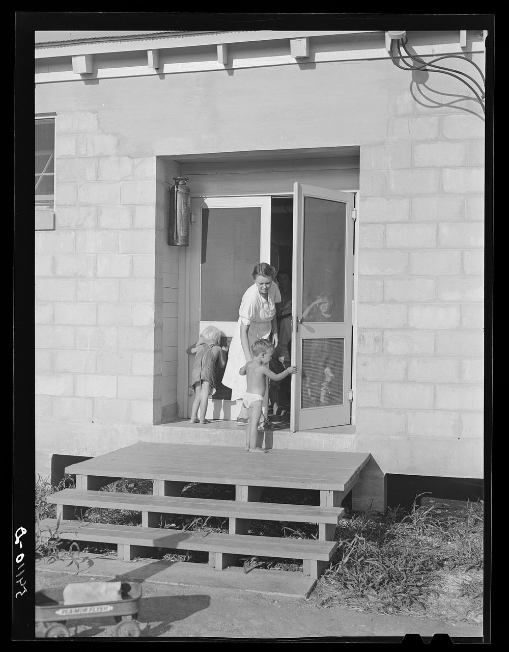 Camp member taking her child into utility building for a shower. Osceola migratory labor camp. Belle Glade, Flordia. Sourced…
