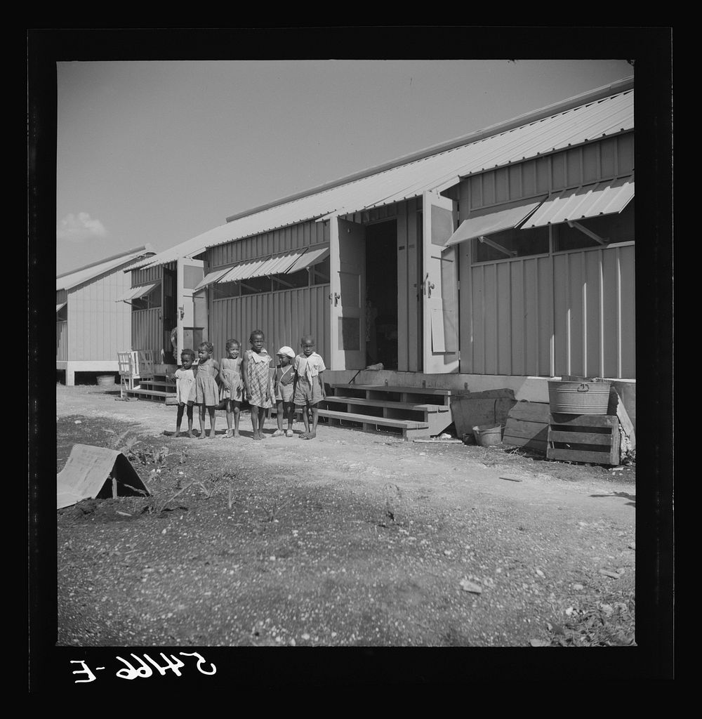 Children of camp members playing outside their shelters in Okeechobee migratory labor camp. Belle Glade, Florida. Sourced…