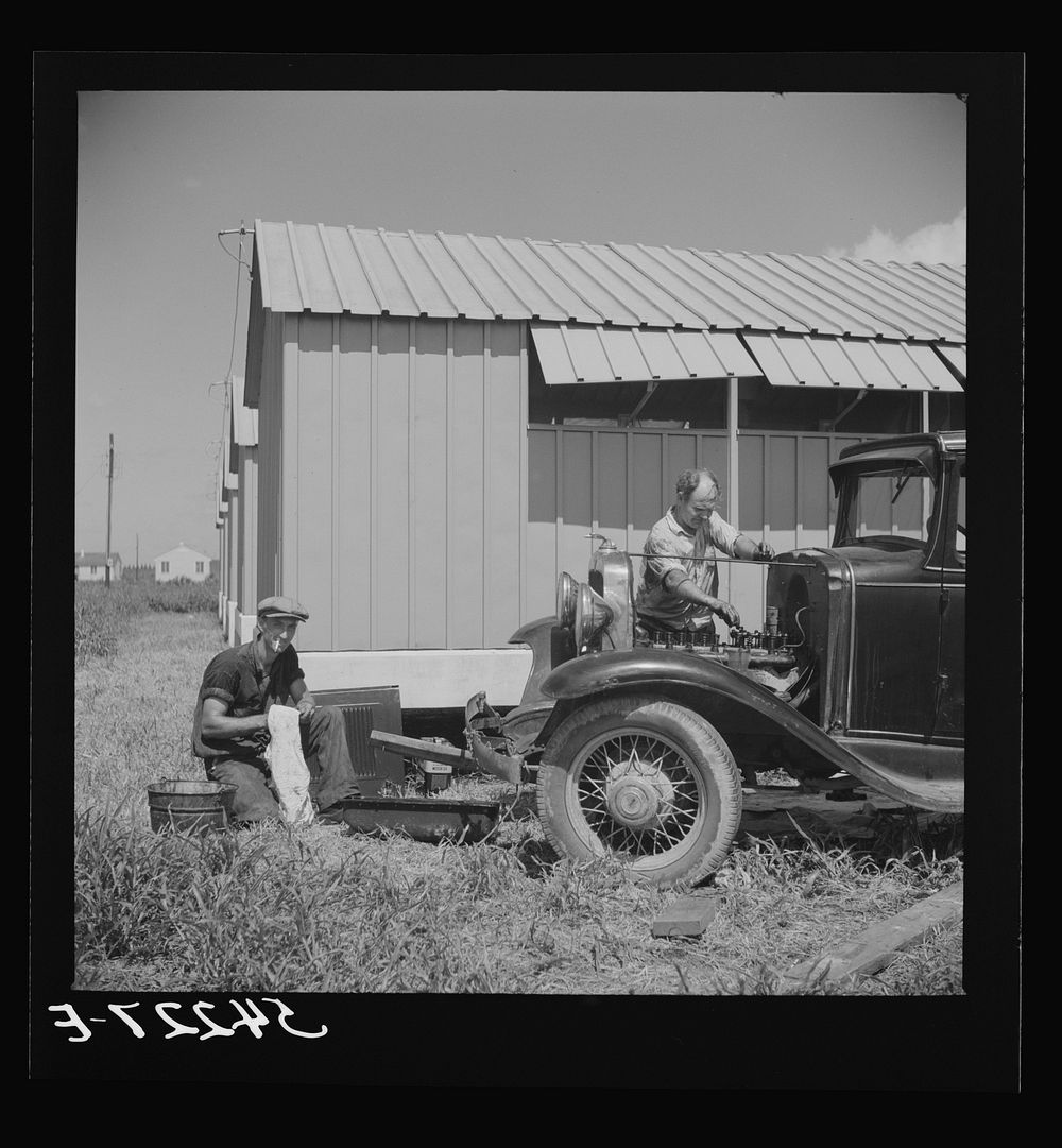 [Untitled photo, possibly related to: Camp member repairing his car outside his shelter. Osceola migratory labor camp. Belle…