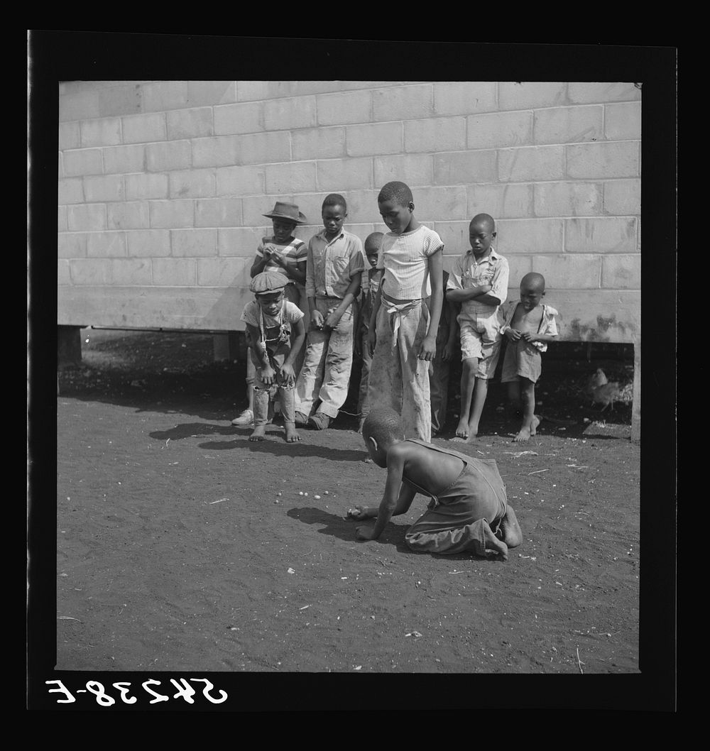 Camp members' children playing marbles outside their shelter units at Okeechobee migratory labor camp. Belle Glade, Florida.…