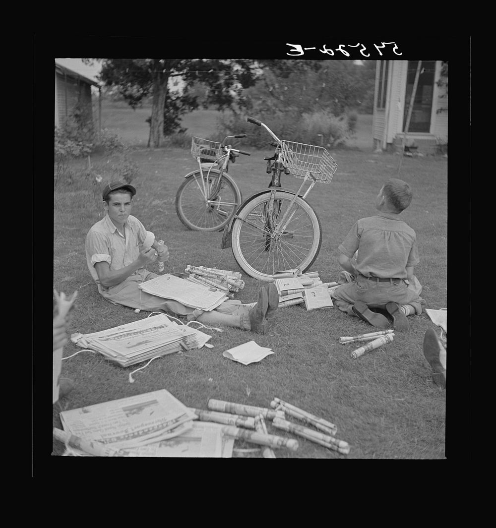 Boys in Natchitoches, Louisiana, folding papers before delivering them in the afternoon. Sourced from the Library of…
