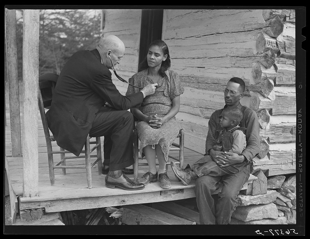 Dr. S.A. Malloy examining Louis Graves and his family on their front porch. They are FSA (Farm Security Administration)…